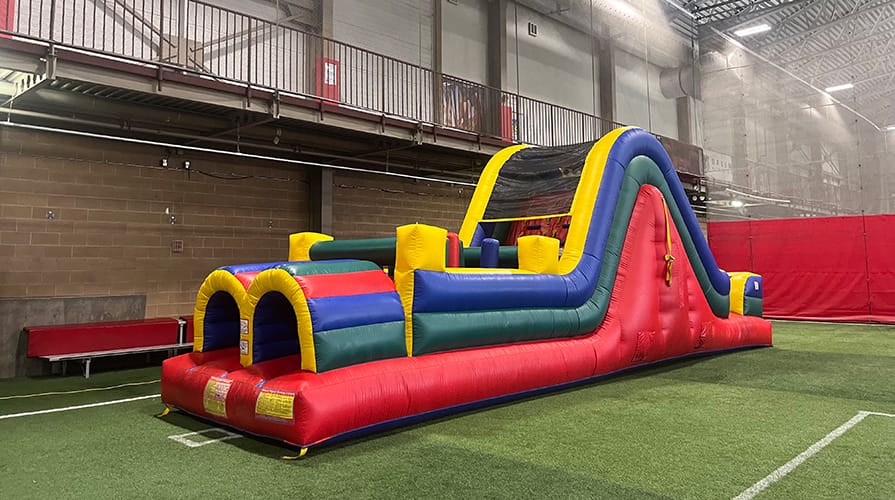 Inflatable obstacle course indoors with colorful arches and a slide.