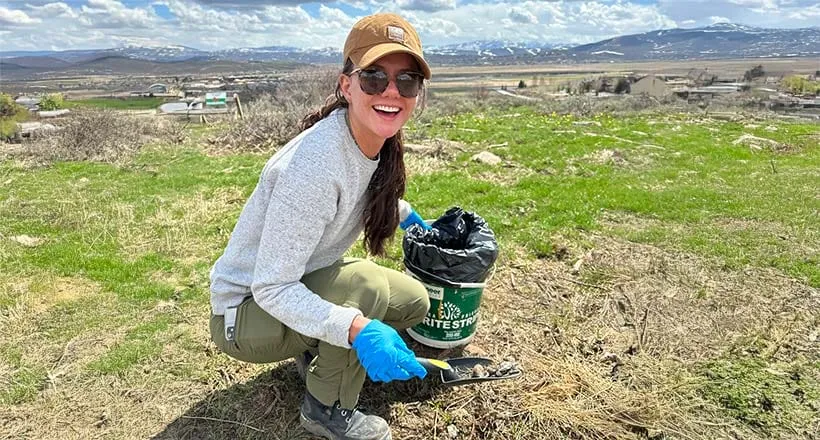 Person gardening outdoors with mountains in the background.