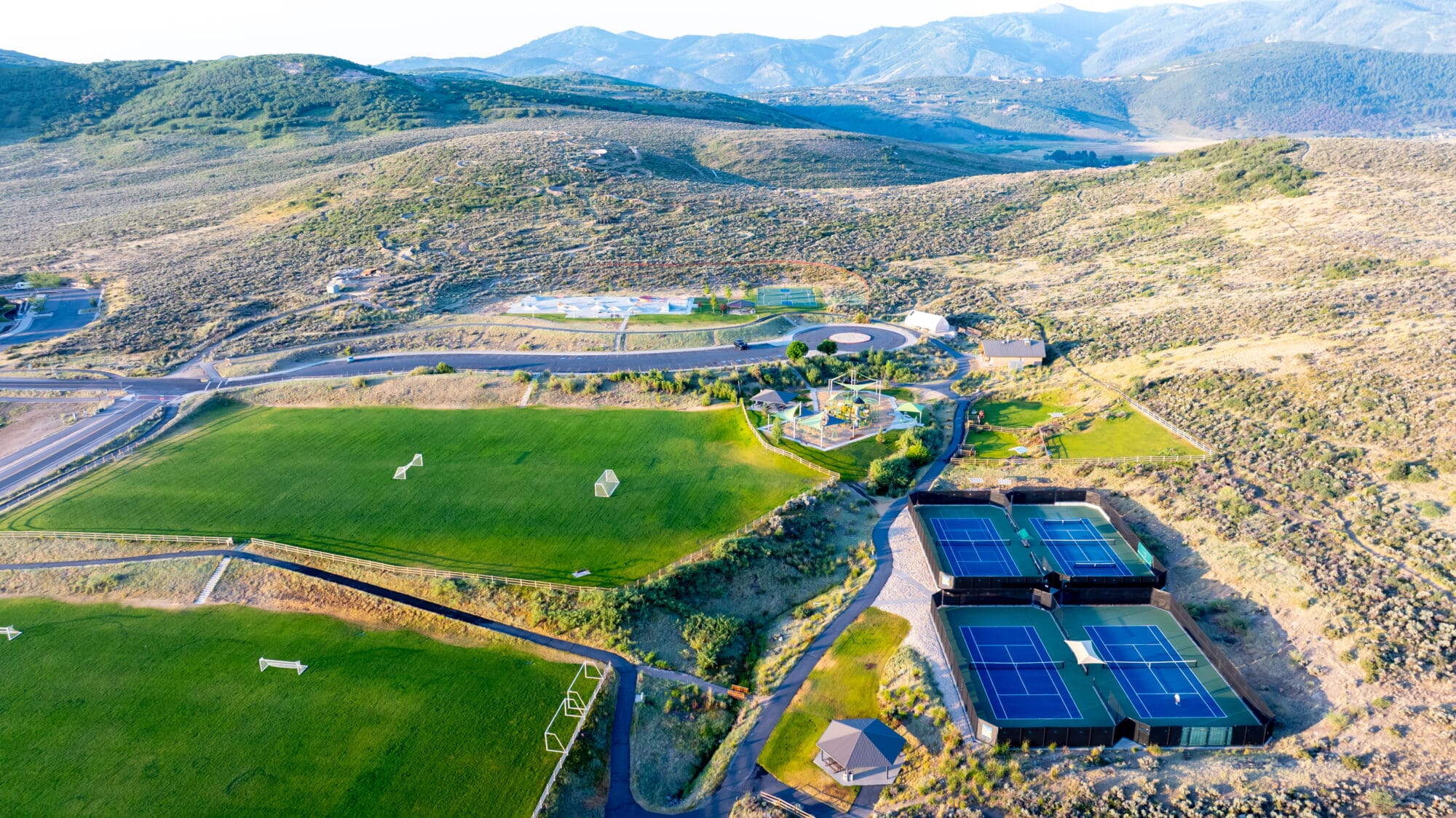 Drone footage of Trailside Park, featuring the tennis and pickleball courts, playing fields, skate park, basketball courts and the bike park. Paved trails border the fields, and single track trails flow through the mountains of sagebrush.