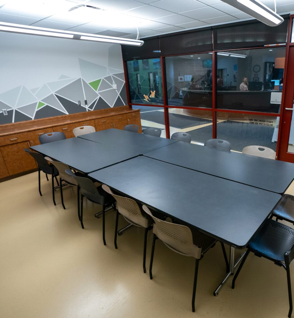 Conference room with a large black table, chairs, geometric mural, and large windows.