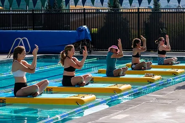 Women practicing yoga on inflatable mats in a swimming pool.