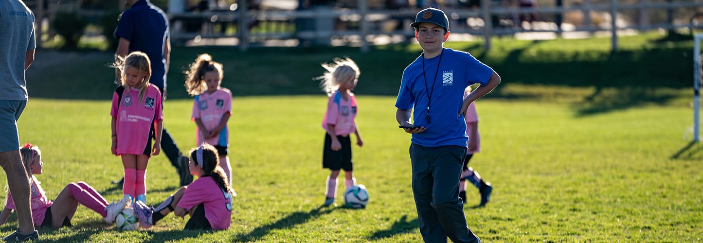 Children in pink sports uniforms on a sunny soccer field with a coach in a blue shirt.