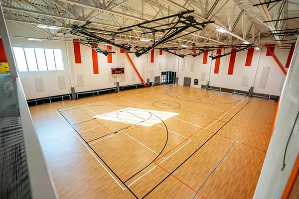 A gymnasium with a wooden floor, basketball hoops, and large windows.