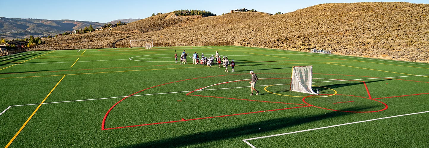 Aerial view of a turf playing field with people on the field, and hills in the background