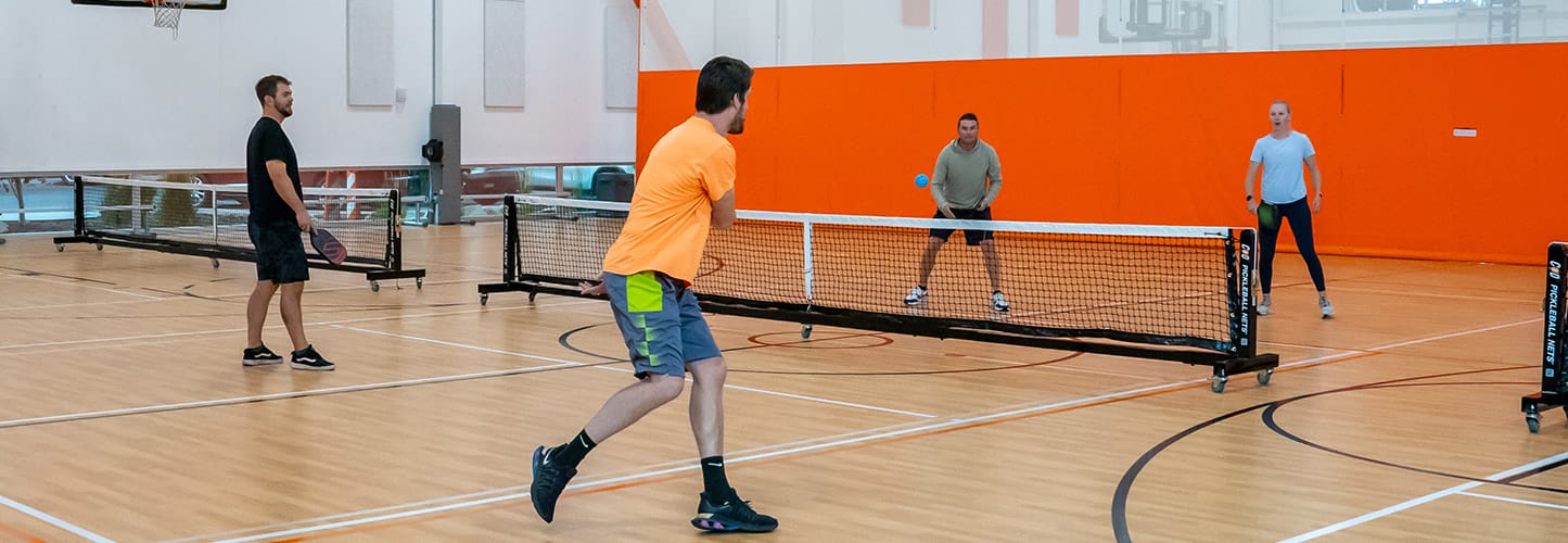 Four people playing pickleball in an indoor gym.