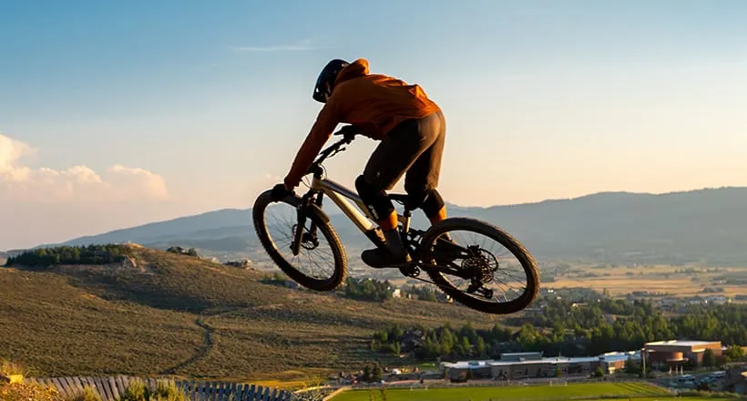 Mountain biker jumping on a trail with a scenic hilly landscape in the background.