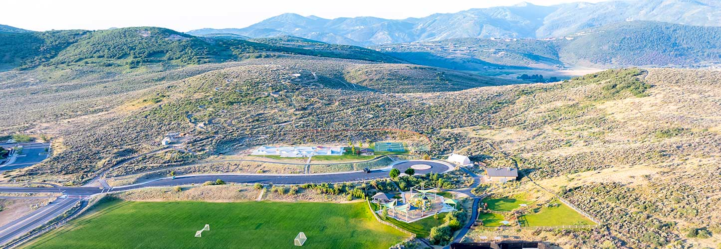 Aerial view of a hilly landscape with a recreational facility, sports field, and mountains in the background.