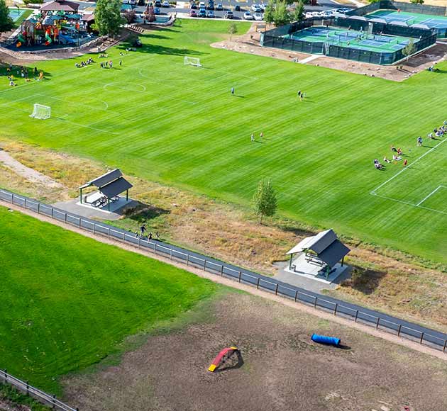 Aerial view of a park with a sports field, playground, tennis courts, and pathways with benches.